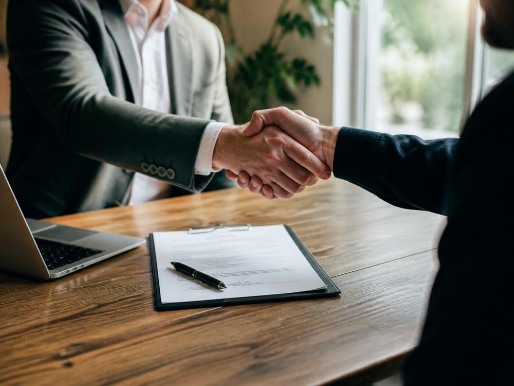 Two people shaking hands over a signed operating agreement at a desk